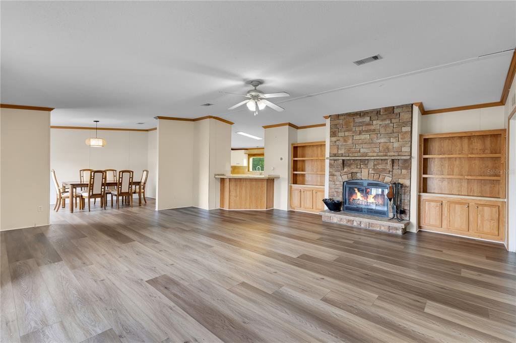 A spacious living room features wood-look flooring, a stone fireplace, and built-in wooden shelving — 410 LAGOON COURT, KENANSVILLE, FL