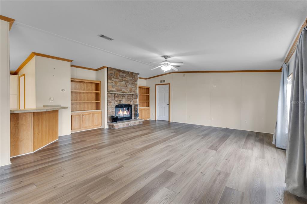 A living room features wood-look flooring, a stone fireplace, built-in shelving, and a ceiling fan — 410 LAGOON COURT, KENANSVILLE, FL