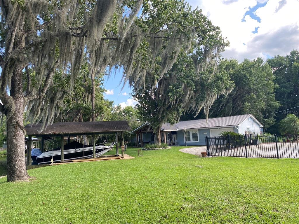 A boat under a covered dock sits on a lawn beside a blue house — 137 & 135 RIVERSIDE DRIVE, SATSUMA, FL