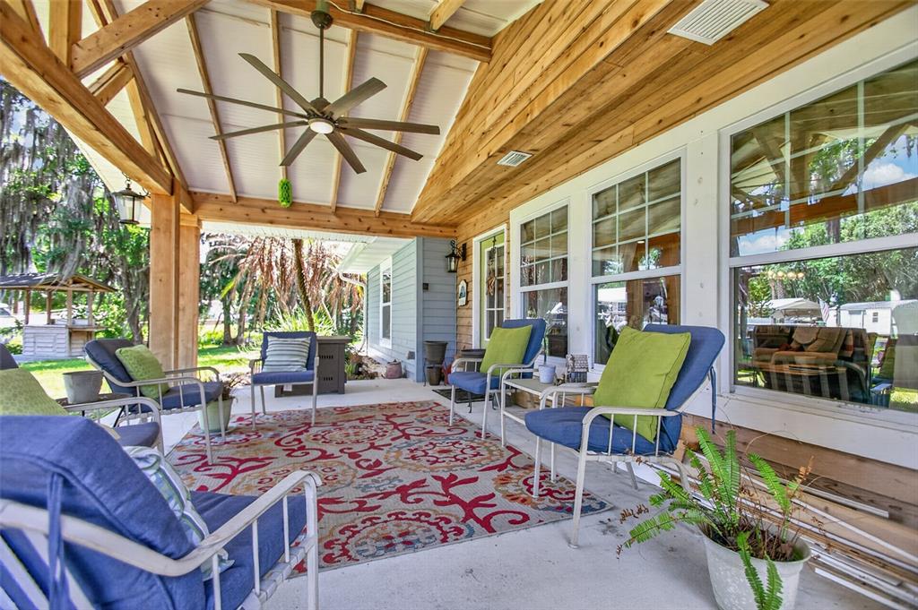A covered patio features a wood-paneled ceiling, a ceiling fan, and blue chairs on a rug — 137 & 135 RIVERSIDE DRIVE, SATSUMA, FL