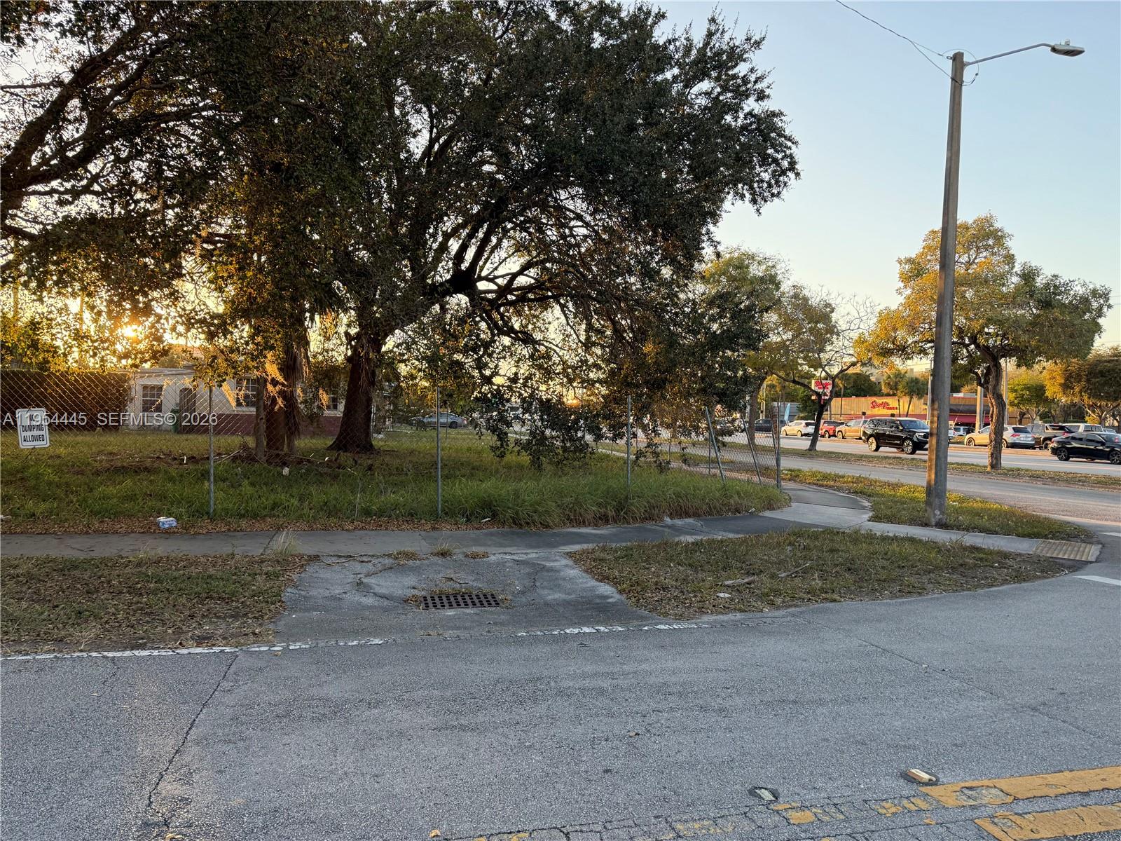 A chain-link fence encloses a grassy lot with a large tree beside a paved road — 11450 SW 40th St, Miami FL 33165, MIAMI, FL