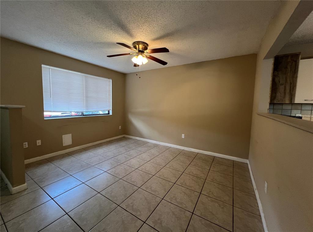 An empty room with beige walls, tile flooring, a ceiling fan, and a large window — 100 E BAYWOOD SQUARE, DAYTONA BEACH, FL