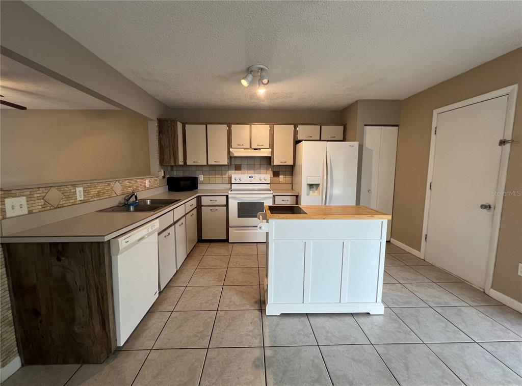 A kitchen features white cabinets, a central island with a wood top, and tiled flooring — 100 E BAYWOOD SQUARE, DAYTONA BEACH, FL