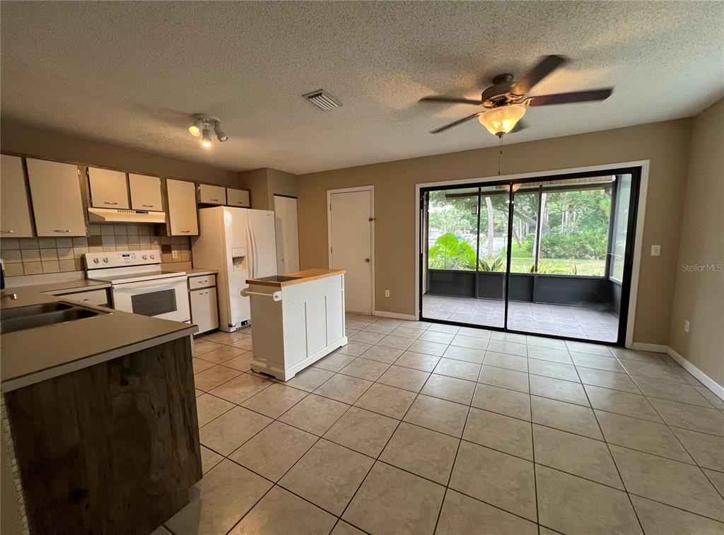 A kitchen with white cabinets, a portable island, and tile flooring leads to a screened patio — 100 E BAYWOOD SQUARE, DAYTONA BEACH, FL