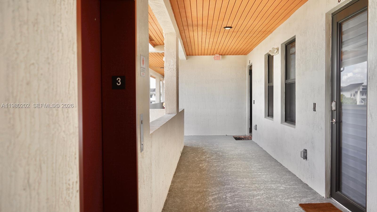 An outdoor apartment hallway features a concrete floor, white stucco walls, and a wood-paneled ceiling — 7925 NW 104th Ave # 32, Doral FL 33178, DORAL, FL