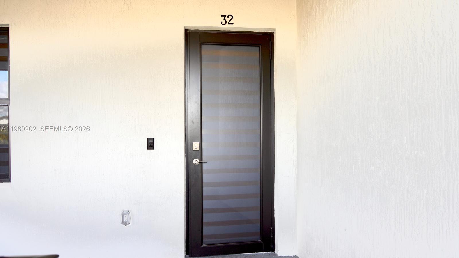 A dark-framed glass door with horizontal blinds is centered on a white exterior wall — 7925 NW 104th Ave # 32, Doral FL 33178, DORAL, FL