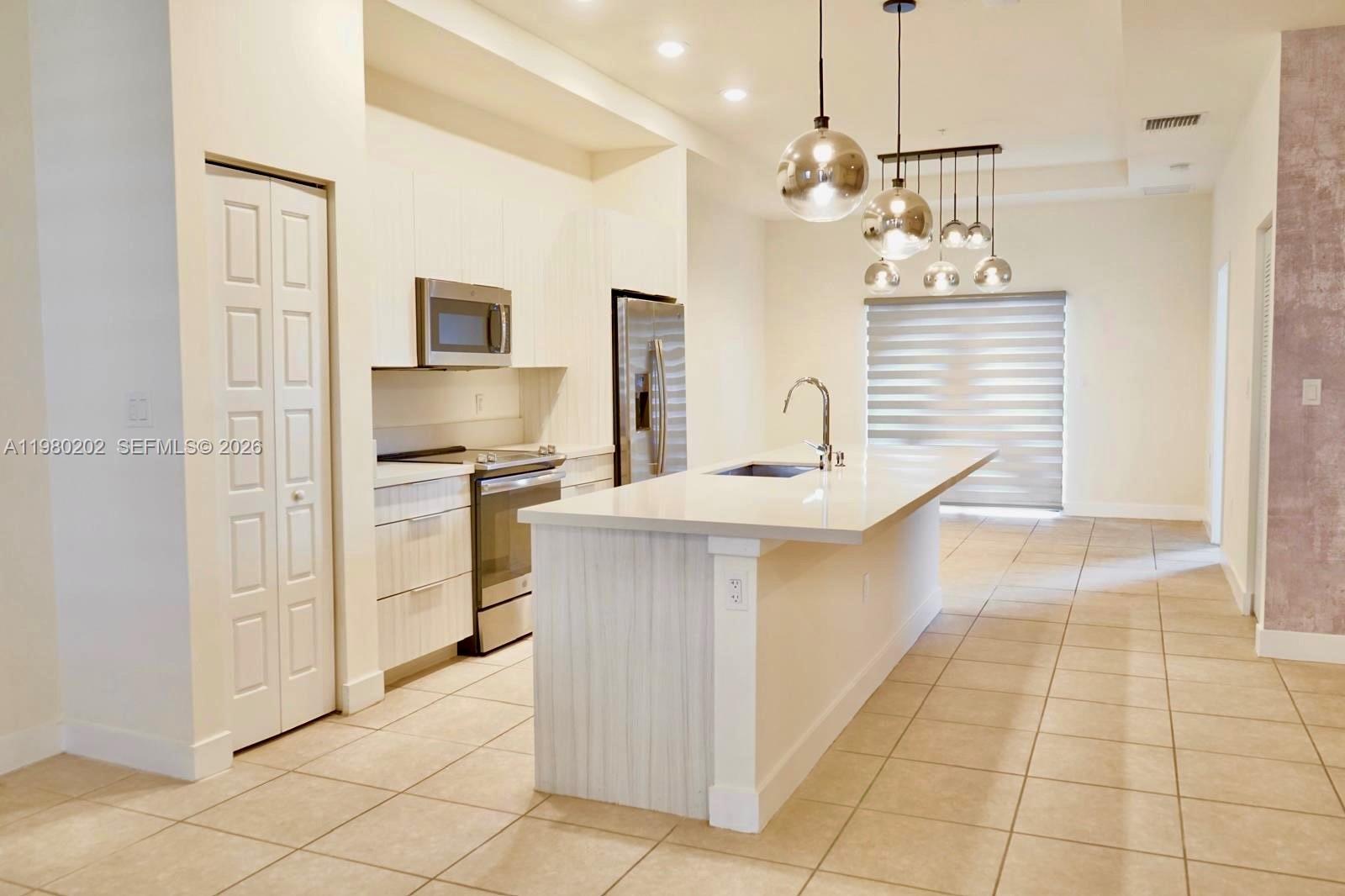 A modern kitchen features white cabinetry, stainless steel appliances, a quartz island, and pendant lighting — 7925 NW 104th Ave # 32, Doral FL 33178, DORAL, FL