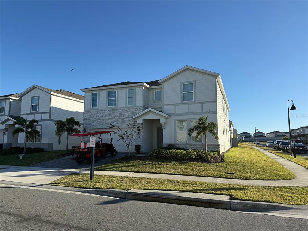 A two-story suburban house with light siding, stone accents, and a golf cart in the driveway — 3029 MAHALO DRIVE, DAVENPORT, FL