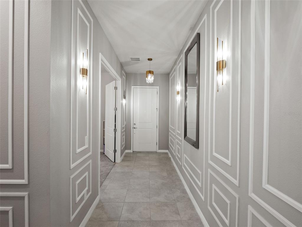 A hallway features gray walls with white molding, tile flooring, and wall-mounted light fixtures — 3367 CANYON GRAND POINT, LONGWOOD, FL