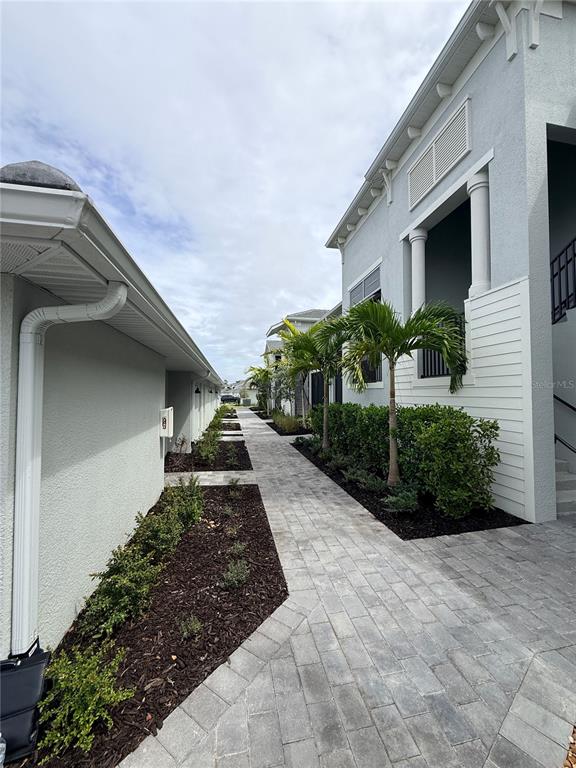 A paved walkway runs between two light-colored buildings with landscaping and palm trees — 15175 BLUFFTON LANE UNIT 724, PUNTA GORDA, FL