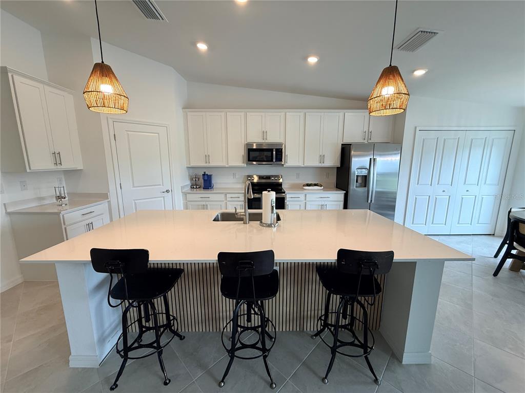 A modern kitchen features a large white quartz island with three black stools and cabinetry — 15175 BLUFFTON LANE UNIT 724, PUNTA GORDA, FL