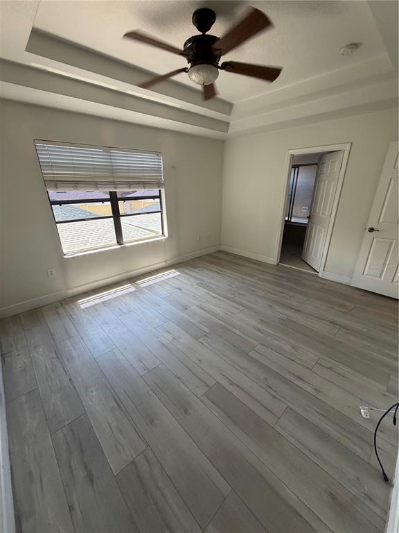 A bedroom features light wood-look flooring, a tray ceiling with a fan, and a window — 4048 VIOSCA PLACE, ORLANDO, FL
