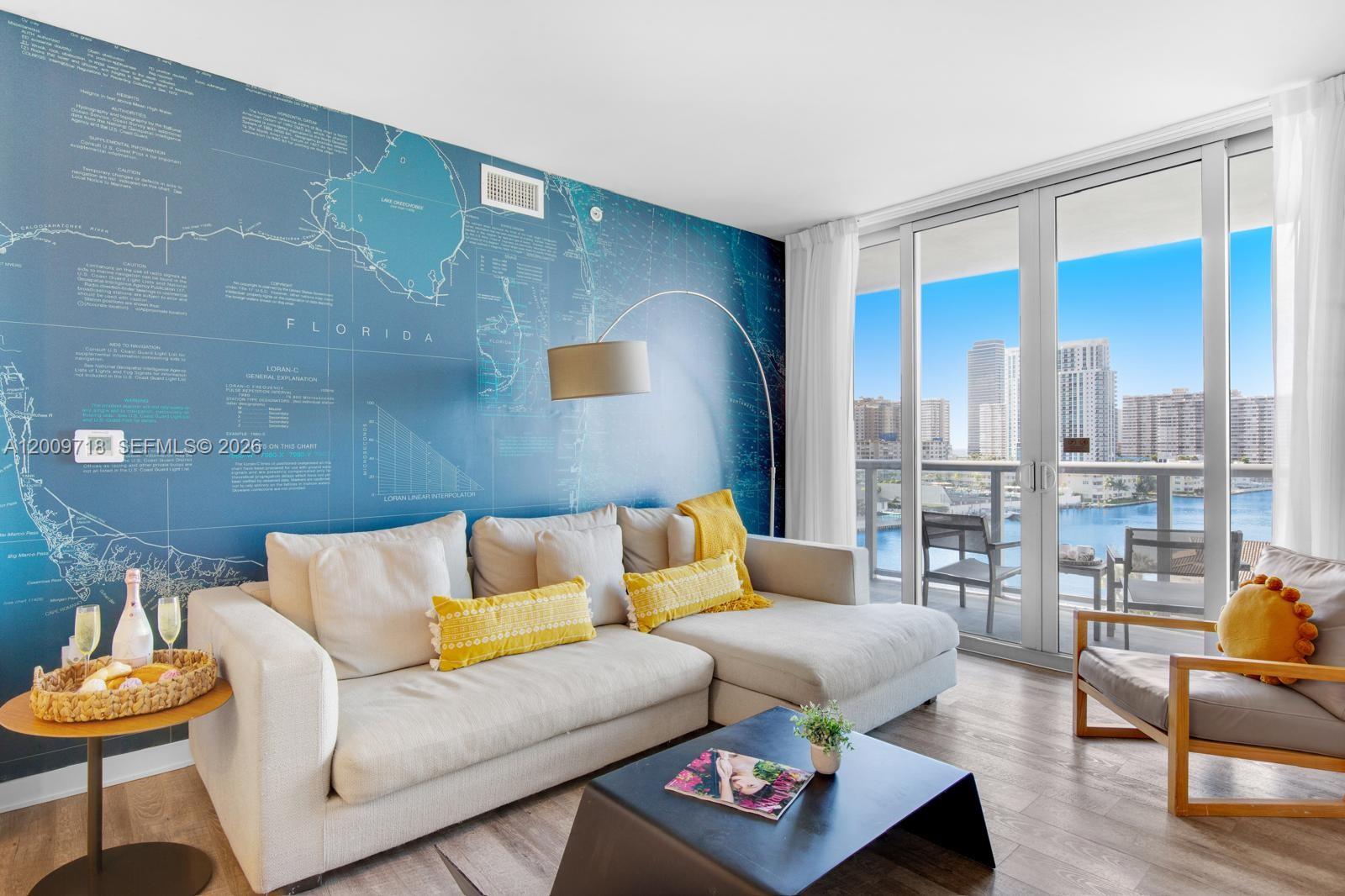 A living room features a blue map-themed accent wall, beige sectional sofa, and balcony view — 2602 E Hallandale Beach Blvd # R803, Hallandale Beach FL 33009, HALLANDALE BEACH, FL