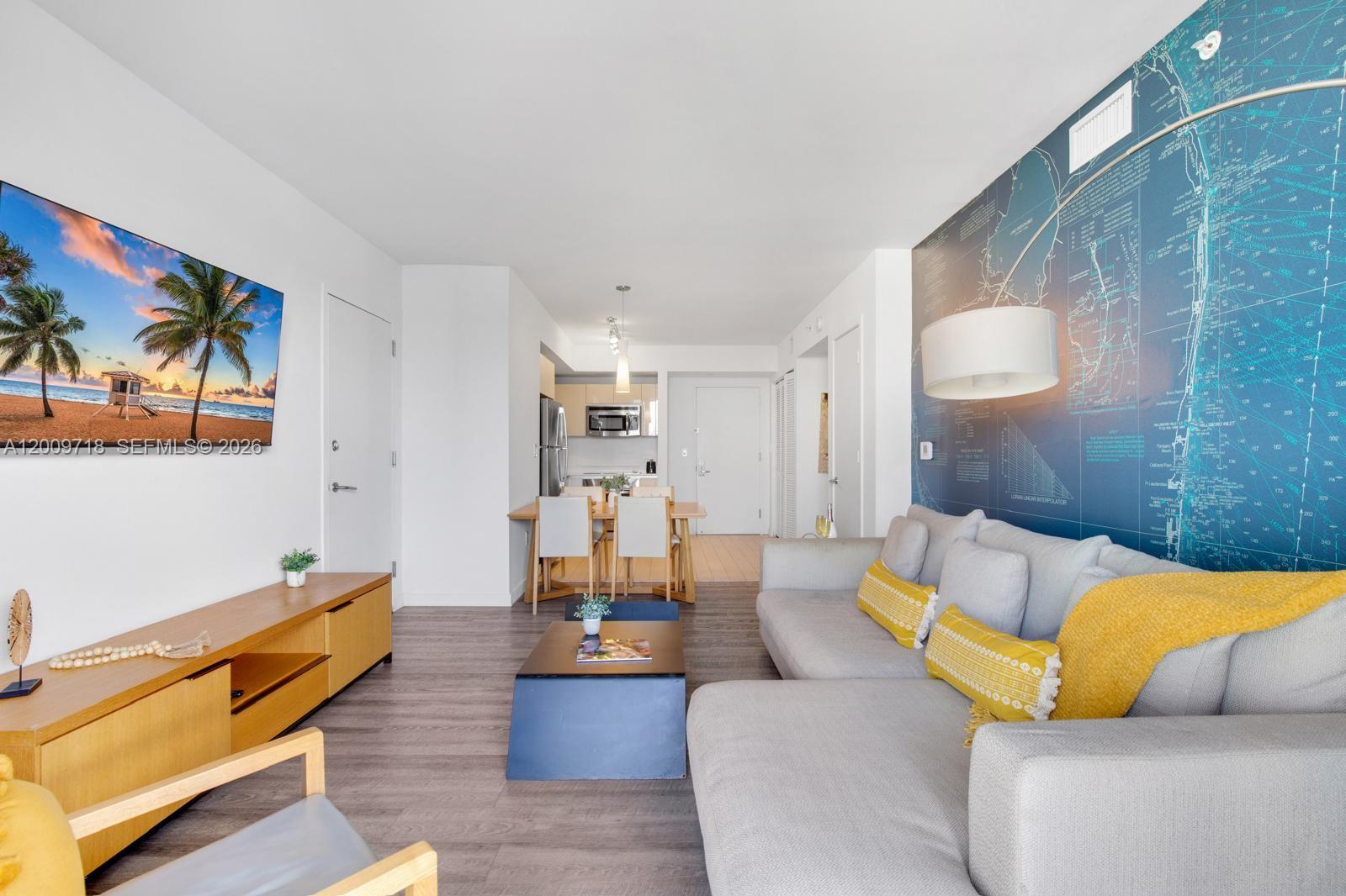 A living room features a grey sectional sofa, a wood media console, and a map mural — 2602 E Hallandale Beach Blvd # R803, Hallandale Beach FL 33009, HALLANDALE BEACH, FL