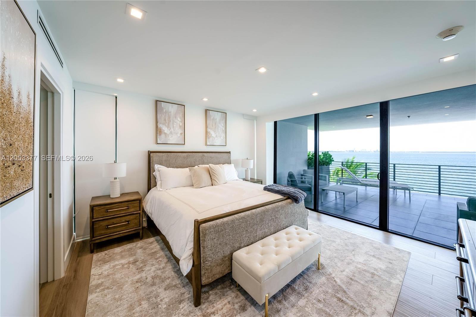 A modern bedroom features a bed, tufted bench, and floor-to-ceiling windows overlooking the ocean — 1930 Bay Dr # 2, Miami Beach FL 33141, MIAMI BEACH, FL
