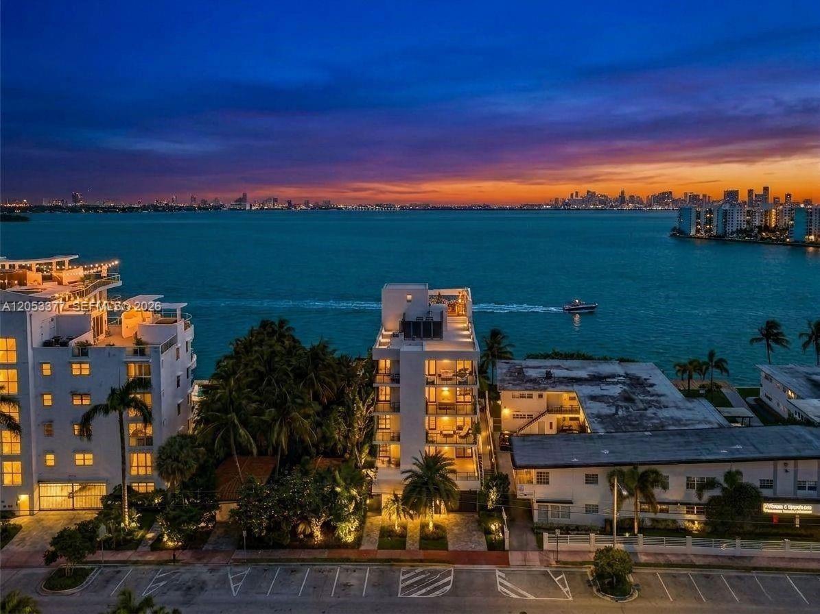 An aerial view of waterfront apartment buildings at dusk with a city skyline in distance — 1930 Bay Dr # 2, Miami Beach FL 33141, MIAMI BEACH, FL
