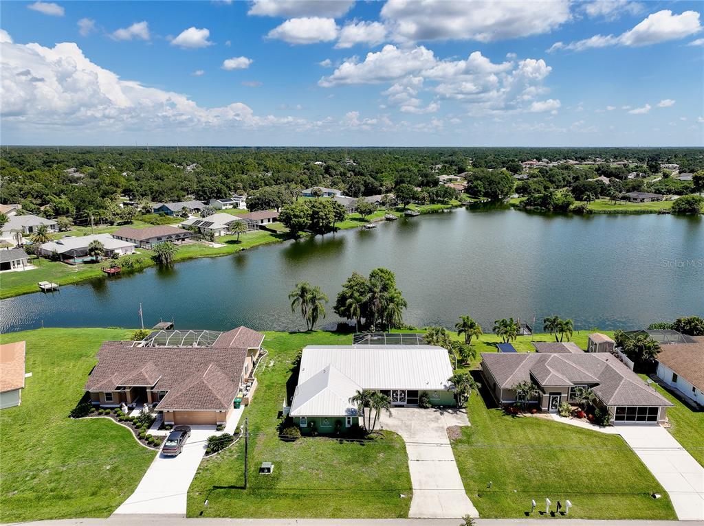 An aerial view shows three suburban houses situated along the edge of a large lake — 22234 TENNYSON AVENUE, PORT CHARLOTTE, FL