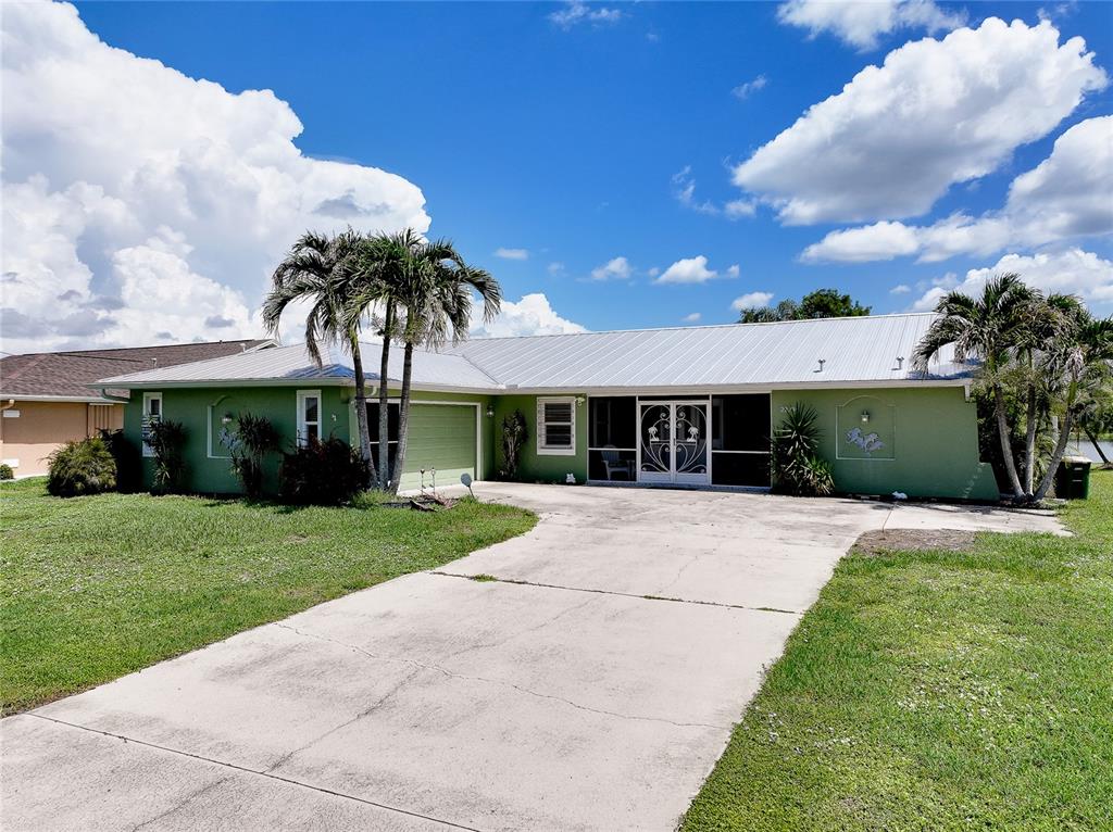 A single-story green house with a metal roof and a concrete driveway under blue skies — 22234 TENNYSON AVENUE, PORT CHARLOTTE, FL