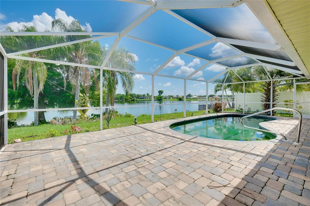 A screened-in patio features a paved deck, a swimming pool, and a view of a lake — 22234 TENNYSON AVENUE, PORT CHARLOTTE, FL