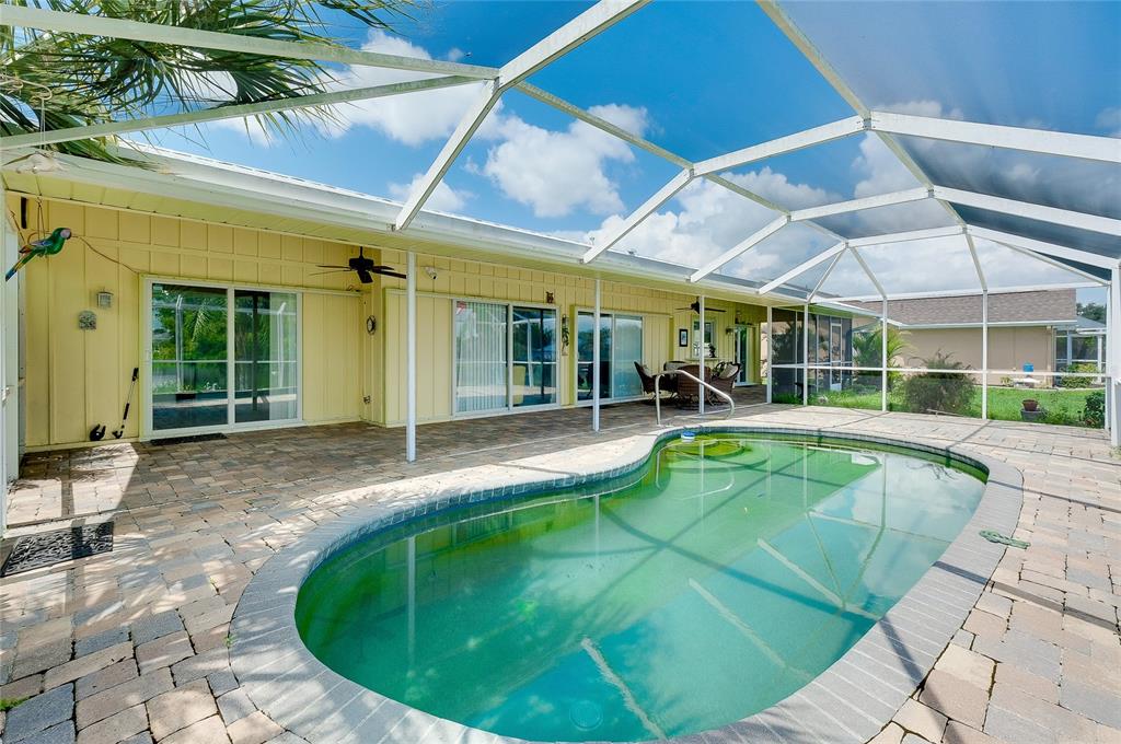 A swimming pool sits on a paved patio enclosed by a screened lanai behind a house — 22234 TENNYSON AVENUE, PORT CHARLOTTE, FL