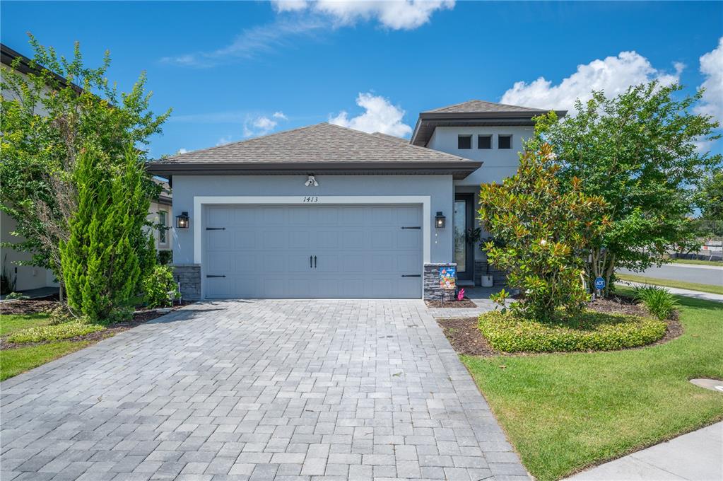 A gray single-story house features a two-car garage, stone accents, and a paved driveway — 1413 BELLAMY DRIVE, REUNION, FL