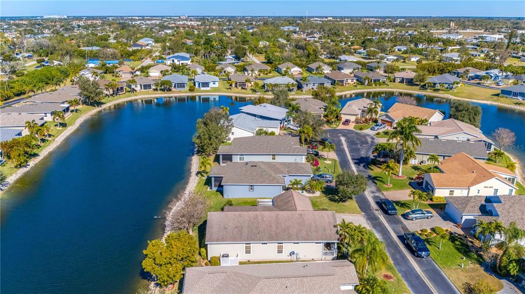 An aerial view shows a suburban neighborhood with houses situated along a winding lake — 8632 LAKE FRONT COURT, PUNTA GORDA, FL