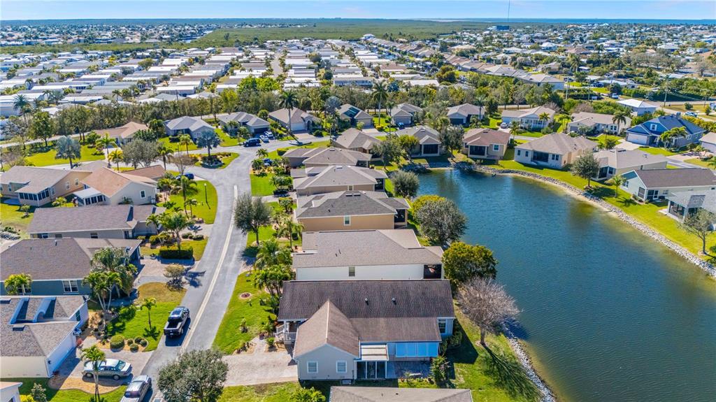 An aerial view shows a suburban neighborhood with houses surrounding a small lake — 8632 LAKE FRONT COURT, PUNTA GORDA, FL