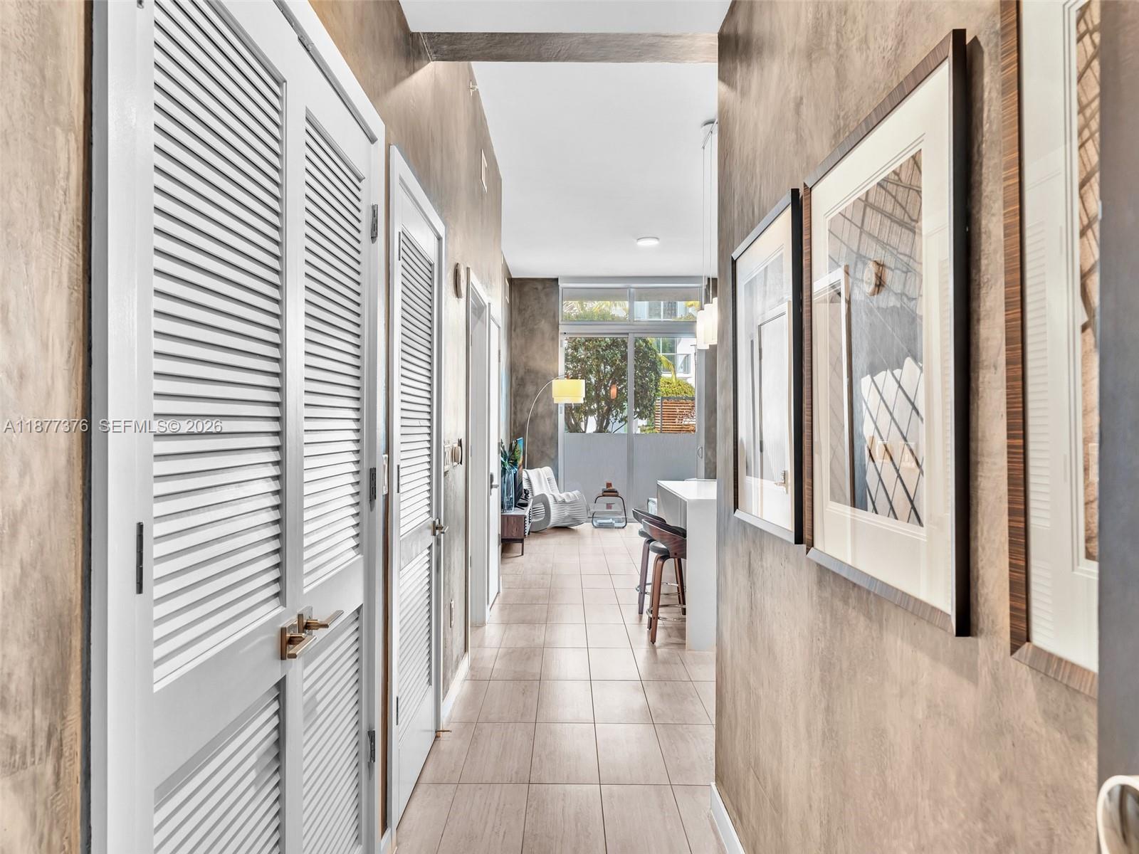 A hallway with louvered closet doors leads to a kitchen and living area with tile floors — 3900 Biscayne Blvd # 616, Miami FL 33137, MIAMI, FL