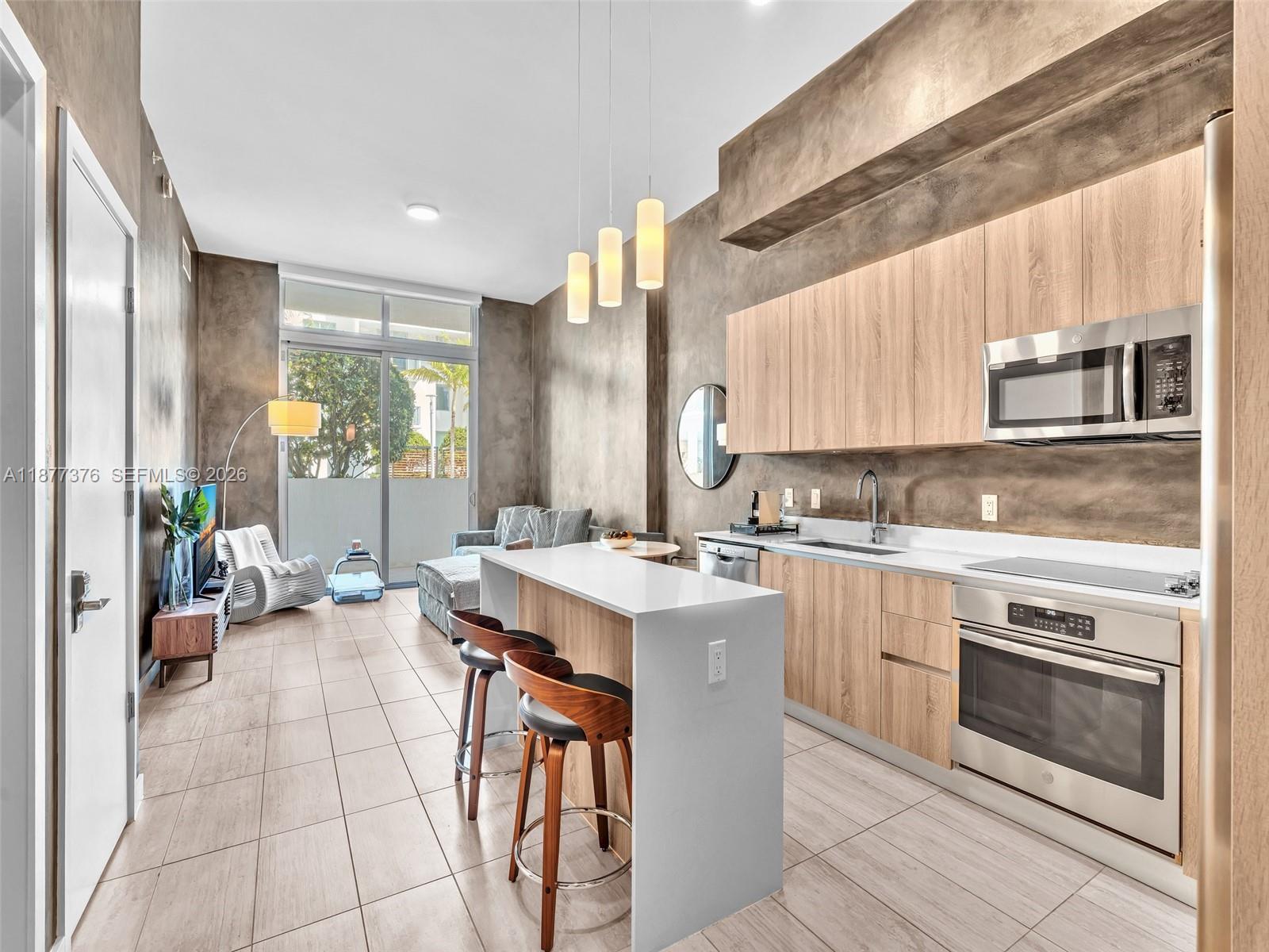 A modern kitchen with light wood cabinets and a white island opens into a living area — 3900 Biscayne Blvd # 616, Miami FL 33137, MIAMI, FL
