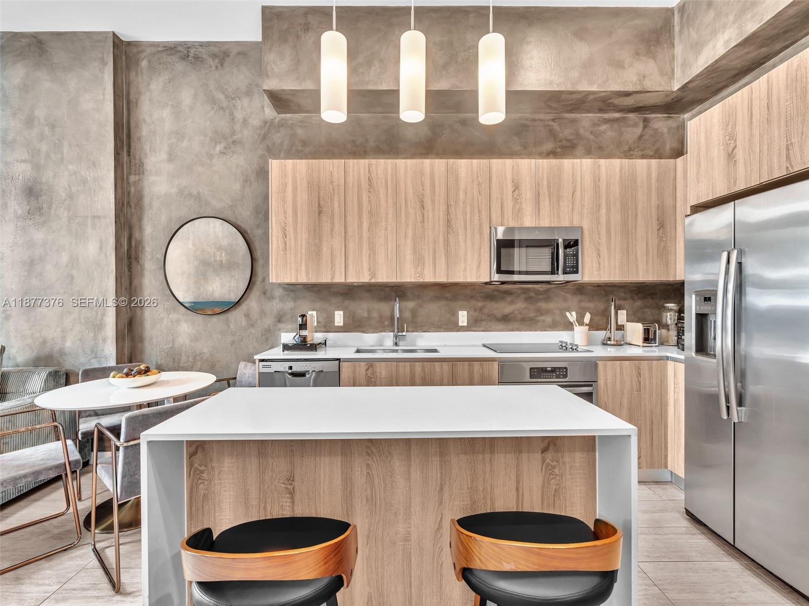 A modern kitchen features light wood cabinets, a white island, and a textured gray wall — 3900 Biscayne Blvd # 616, Miami FL 33137, MIAMI, FL