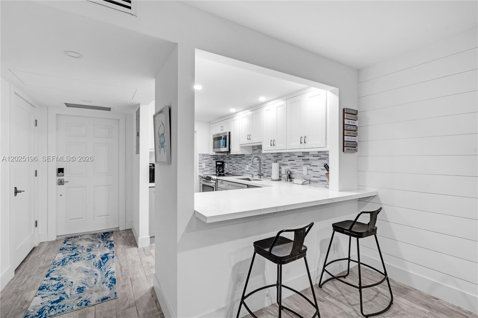 A white kitchen with a breakfast bar and two stools sits beside an entryway — 4502 N Federal Hwy # 167H, Lighthouse Point FL 33064, LIGHTHOUSE POINT, FL