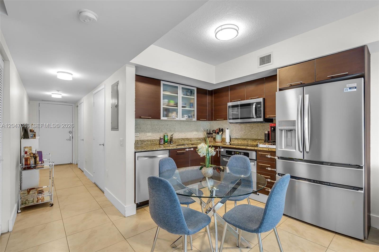A kitchen features dark wood cabinets, stainless steel appliances, granite countertops, and a glass dining table — 41 SE 5th St # 908, Miami FL 33131, MIAMI, FL