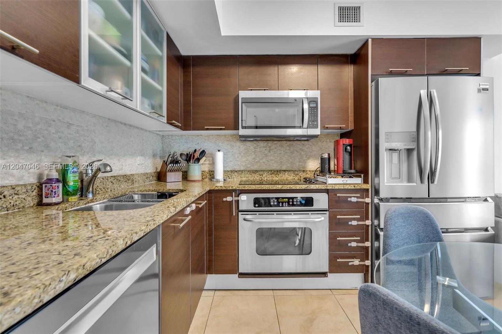 A kitchen features dark wood cabinets, granite countertops, stainless steel appliances, and tile flooring — 41 SE 5th St # 908, Miami FL 33131, MIAMI, FL