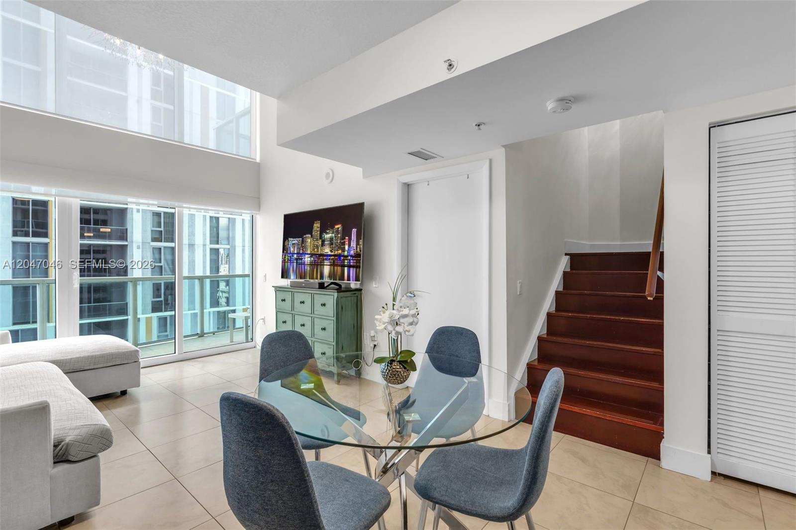 A dining area with a glass table and blue chairs sits beside a wooden staircase — 41 SE 5th St # 908, Miami FL 33131, MIAMI, FL