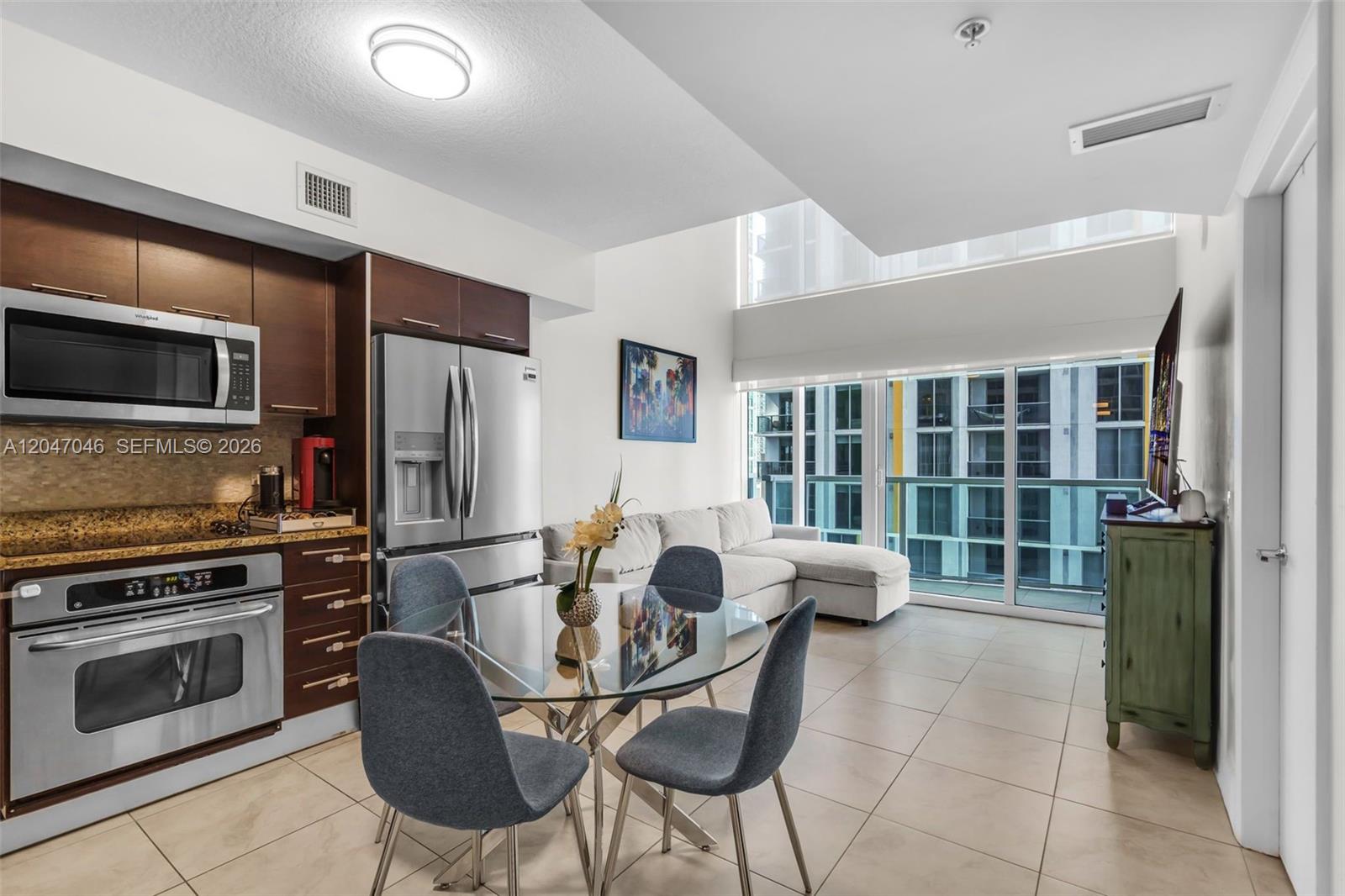 A modern kitchen and dining area with stainless steel appliances, a glass table, and balcony views — 41 SE 5th St # 908, Miami FL 33131, MIAMI, FL
