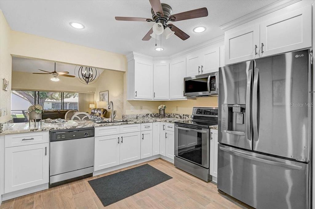 A kitchen features white cabinets, stainless steel appliances, granite countertops, and wood-look tile flooring — 892 COUNTRY CLUB CIRCLE UNIT 50, VENICE, FL
