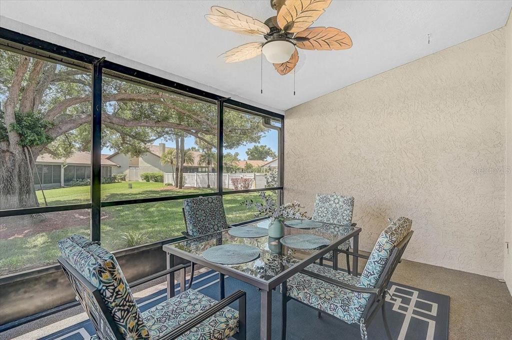 A screened-in patio features a glass-top dining table, four patterned chairs, and a ceiling fan — 892 COUNTRY CLUB CIRCLE UNIT 50, VENICE, FL
