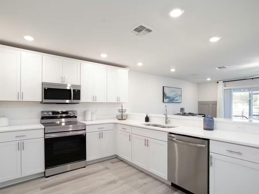 A modern kitchen features white cabinets, stainless steel appliances, and light wood-look flooring — 362 CHESAPEAKE DRIVE, ST CLOUD, FL