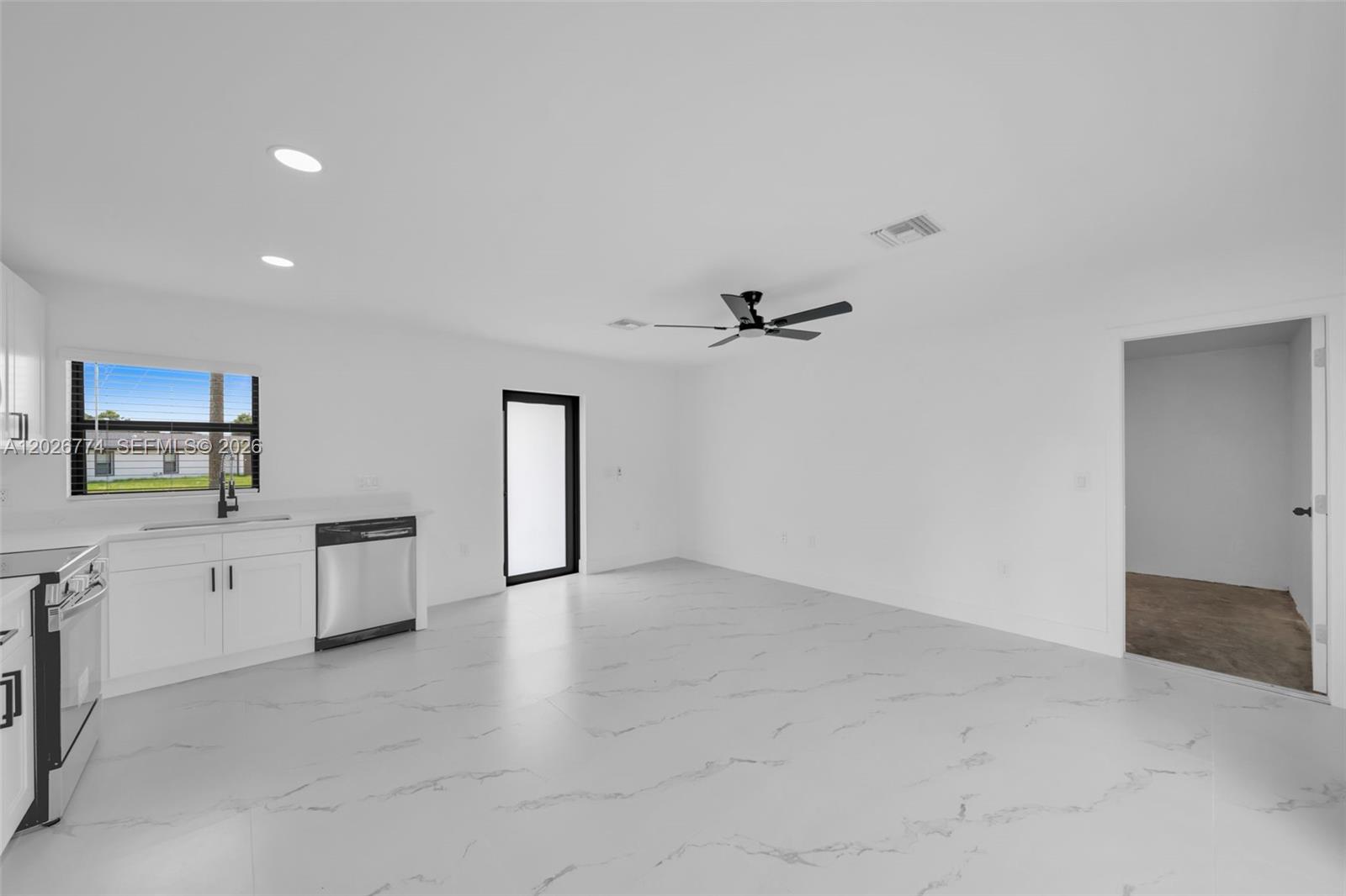 A bright, minimalist kitchen and living area features white cabinetry, marble-look tile floors, and a ceiling fan — 4984 Fairway Ct # 4984, Lehigh Acres FL 33171, LEHIGH ACRES, FL