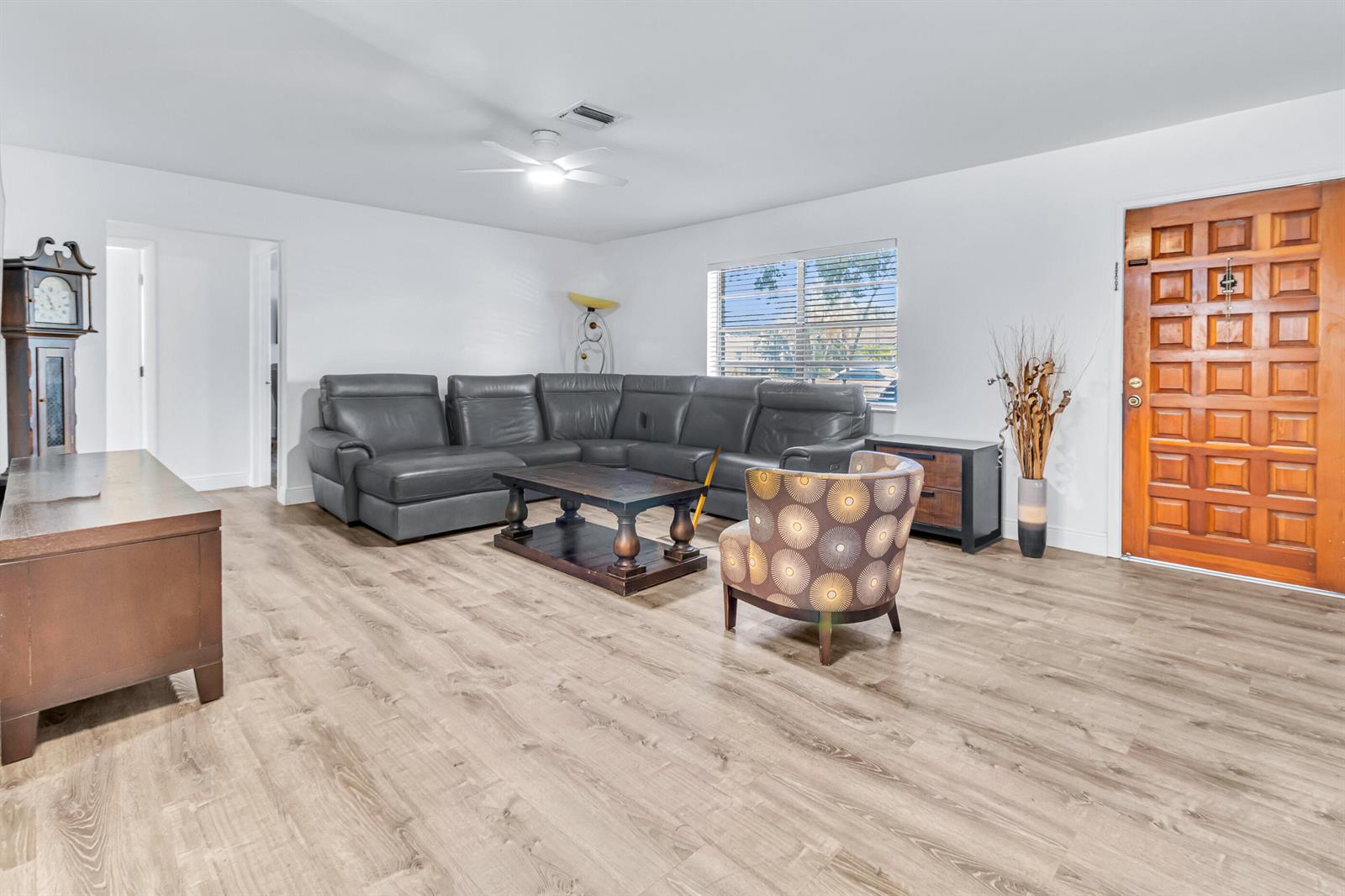 A living room features light wood-look flooring, a grey sectional sofa, and a patterned armchair — 4469 Brandon Drive, Delray Beach FL 33445, DELRAY BEACH, FL