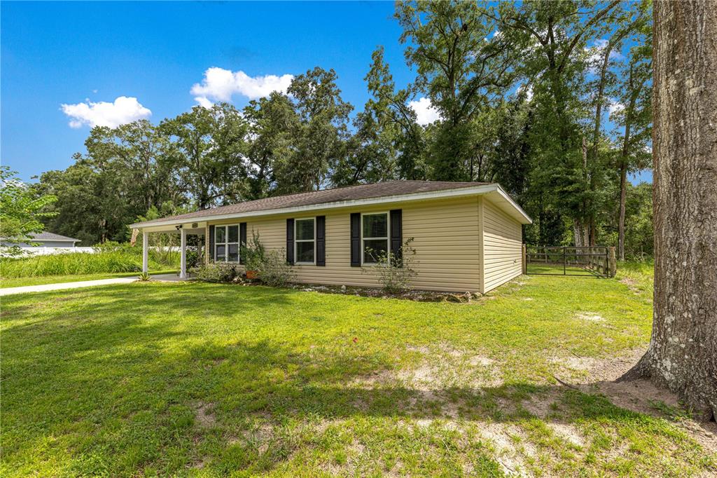 A tan, single-story house with a covered porch sits on a grassy lot with trees — 6353 NW 52ND AVENUE, OCALA, FL