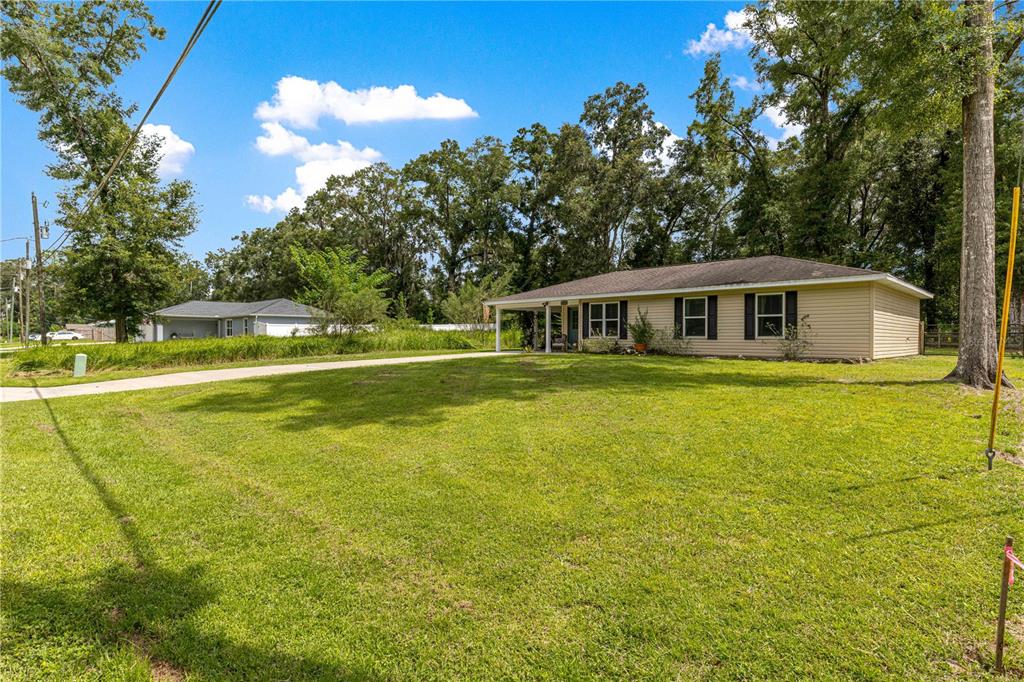 A single-story house with tan siding and a covered porch sits on a grassy lot — 6353 NW 52ND AVENUE, OCALA, FL