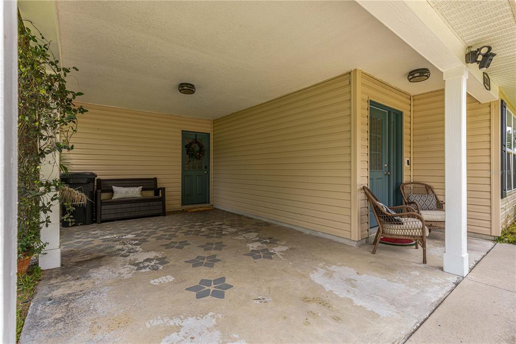 A covered concrete porch features a patterned floor, two doors, and outdoor seating — 6353 NW 52ND AVENUE, OCALA, FL