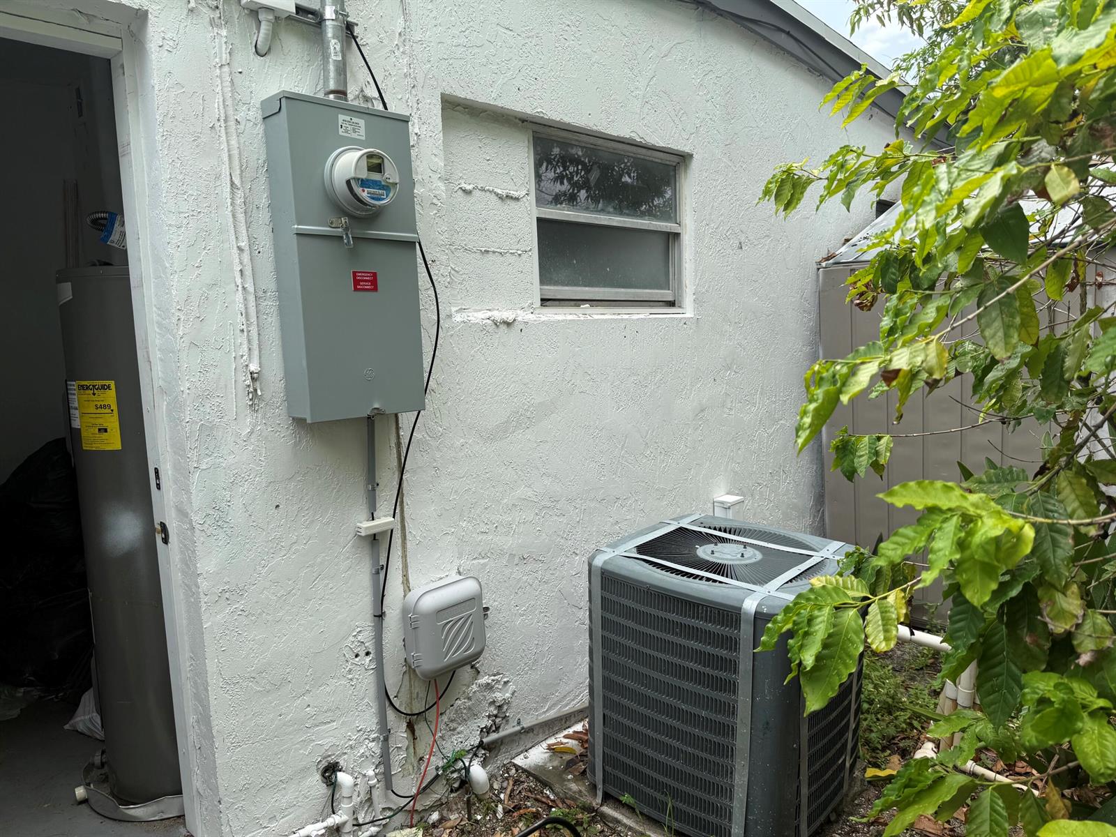 An exterior view of a house wall featuring an electrical meter, HVAC unit, and window — 440 Tulip Tree Drive, Lake Worth FL 33462, LAKE WORTH, FL