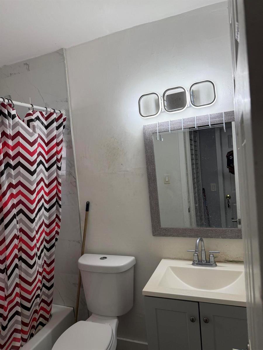 A bathroom features a vanity with a sink, a toilet, a shower, and wall lighting — 440 Tulip Tree Drive, Lake Worth FL 33462, LAKE WORTH, FL