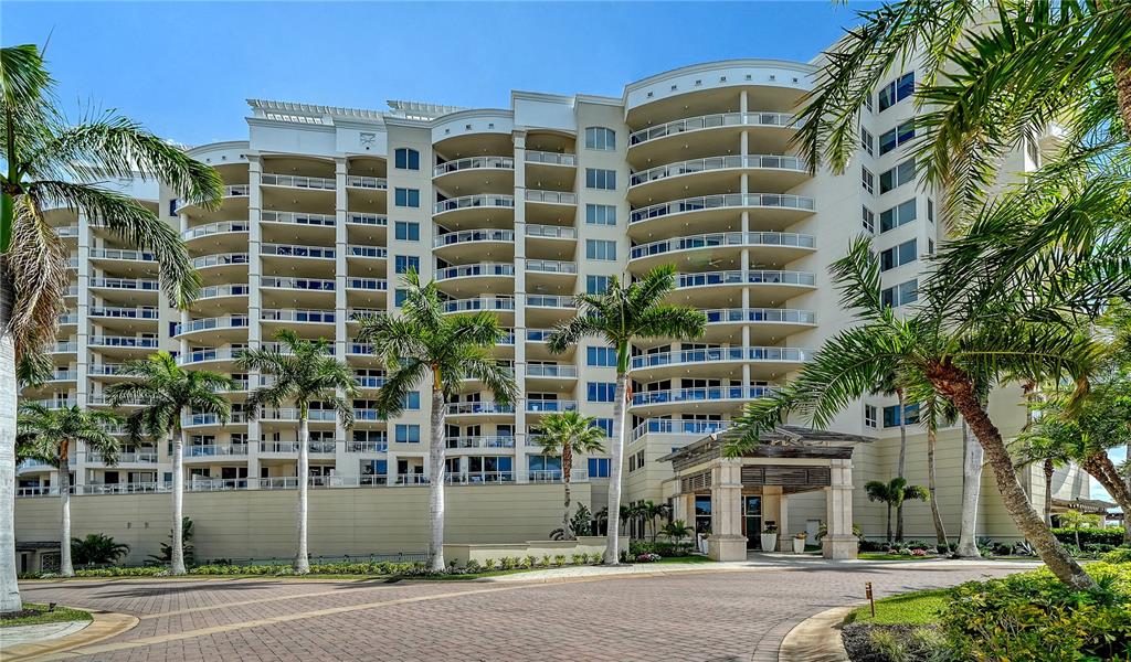 A large, multi-story residential building features curved balconies and a covered entrance with palm trees — 1300 BENJAMIN FRANKLIN DRIVE UNIT 1205 & 1206, SARASOTA, FL