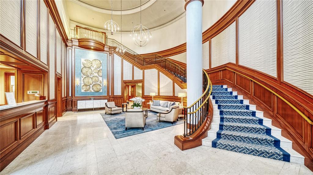 A grand hotel lobby features a curved staircase, wood paneling, and a blue area rug — 1300 BENJAMIN FRANKLIN DRIVE UNIT 1205 & 1206, SARASOTA, FL