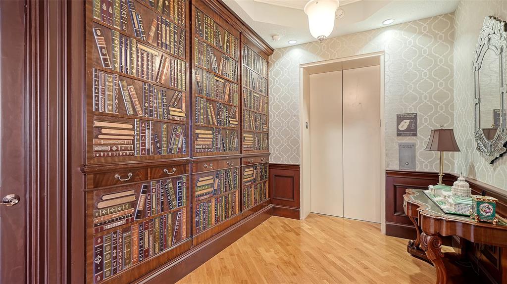 A hallway features wood-paneled walls with faux-bookcase wallpaper, hardwood floors, and a modern elevator — 1300 BENJAMIN FRANKLIN DRIVE UNIT 1205 & 1206, SARASOTA, FL