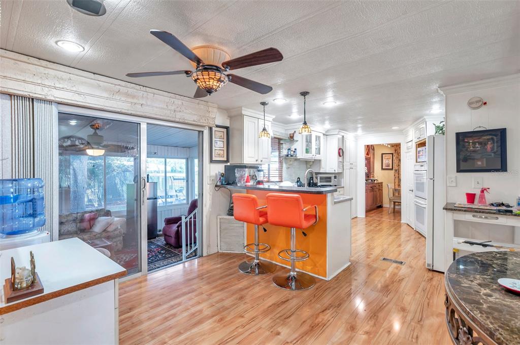 A kitchen with orange bar stools, wood-look flooring, and a sliding glass door to a patio — 6524 ROOSEVELT DRIVE, PORT RICHEY, FL