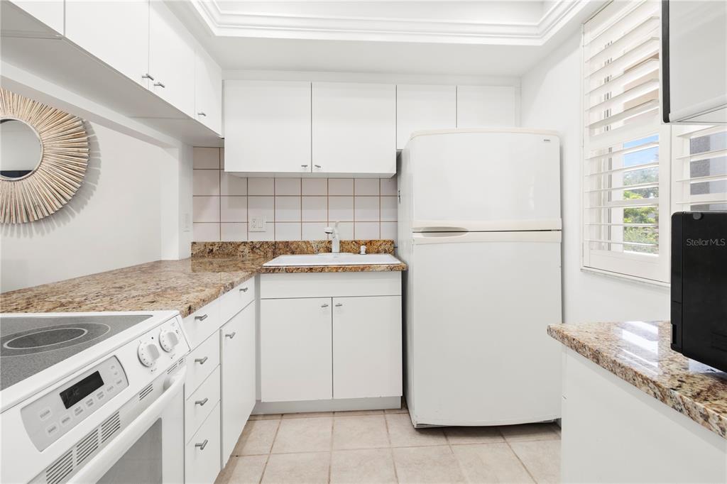 A small kitchen features white cabinets, granite countertops, a white refrigerator, and a sink — 4340 FALMOUTH DRIVE UNIT D-204, LONGBOAT KEY, FL